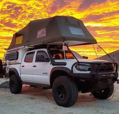 a white truck parked in the desert with a tent on it's roof at sunset