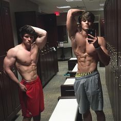 two young men standing in lockers with their hands on their head and looking at their cell phones