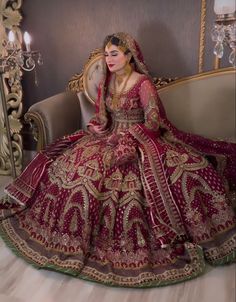 a woman in a red and gold wedding dress sitting on a couch with a mirror behind her