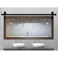 two sinks under a large mirror with lights hanging from the wall above them and below it