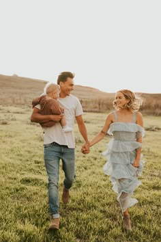 a man and woman holding hands while walking through the grass with a baby in their arms