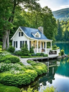 a small white house sitting on top of a lush green hillside next to a lake