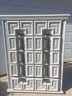 an ornate white cabinet is sitting on the side of a building with two garage doors behind it