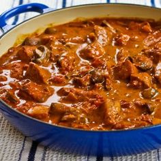 a blue pot filled with meat and sauce on top of a cloth covered tablecloth