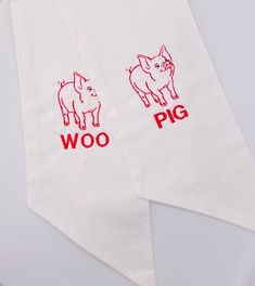 two white tea towels with red words on them, one has a pig and the other has a dog