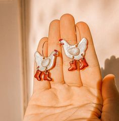 a hand holding two small silver and red bird earrings