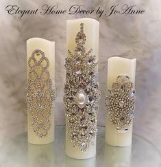 three candles are adorned with crystal and pearl brooches, one candle has an intricate design on it