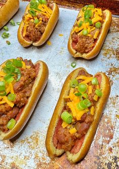 six chili dogs with cheese and green onions on a baking sheet, ready to be eaten