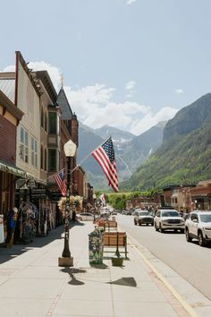 an american flag flying in the wind on a town street with mountains in the background