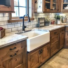 a kitchen with wooden cabinets and marble counter tops, an apron style sink in the center