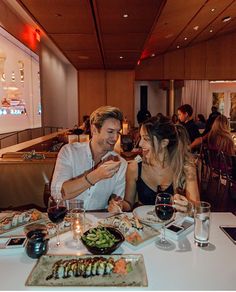 a man and woman sitting at a table with food in front of them on their cell phones