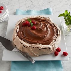 a cake with chocolate frosting and raspberries on a plate next to a fork