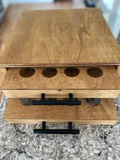 a wooden box with four holes in it on top of a carpeted floor next to a window