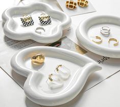 three white trays with gold and silver jewelry on top of each one, sitting on a table