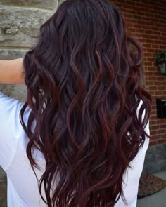 the back of a woman's head with long, wavy hair in front of a brick wall