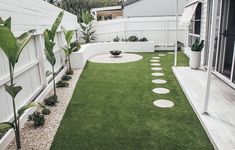 a backyard with grass and stepping stones on the ground, surrounded by white fenced in area