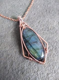 a wire wrapped pendant with a labradorite stone in the center on a gray surface