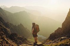 a person with a backpack standing at the top of a mountain looking down on some mountains