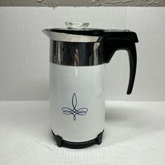 a black and white coffee pot with a handle sitting on top of a white table