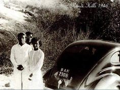 three people standing next to an old car