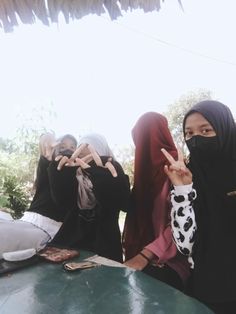 several women in hijabs are sitting at a table and making the peace sign