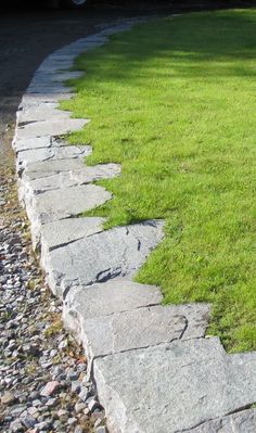 a stone path in the middle of a grassy area next to a parked car on a street