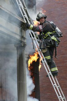 a firefighter climbing up the side of a tall building with his ladder on fire