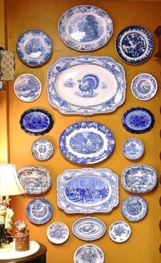 blue and white plates hanging on the wall next to a table with a lamp in front of it