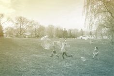 two children are playing with bubbles in the grass while another child is running towards them