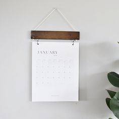 a calendar hanging on a wall next to a potted plant with a wooden hanger