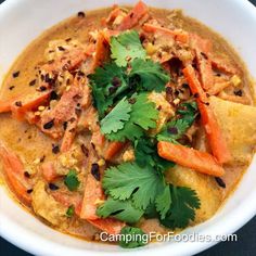 a white bowl filled with food and garnished with cilantro, carrots and parsley