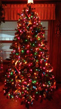 a brightly lit christmas tree in front of a window