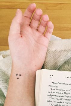 a woman's hand with a tiny star tattoo on her wrist next to an open book