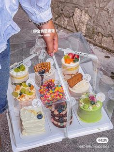 a person is holding a clear plastic tray with cakes on it and other desserts