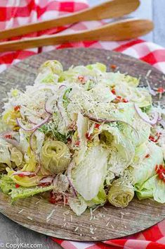 a wooden plate filled with lettuce and onions on top of a checkered table cloth