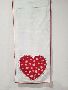 a red and white heart is hanging on the wall next to a piece of cloth