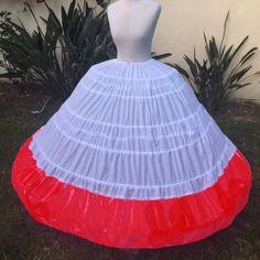 a mannequin wearing a white and red dress on display in front of some plants