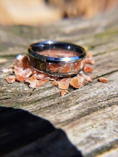 a wedding ring sitting on top of a piece of wood next to some broken leaves