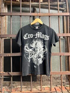 a black shirt hanging on a metal bar in front of a barred door with the word cro - mags printed on it