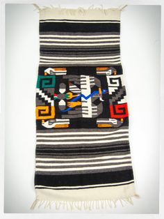 a black and white striped rug with colorful geometric designs on the front, fringes hanging from it's sides