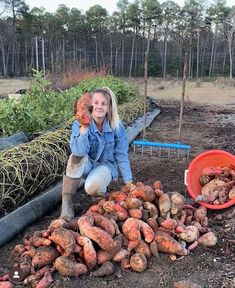 a woman kneeling down in the dirt next to some carrots and other produce items