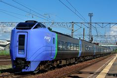 a blue train traveling down tracks next to a loading platform with power lines in the background