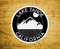 the lake tahoe california sticker is shown on a wooden surface, with mountains in the background