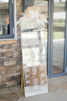 a wedding seating chart on display in front of a stone building with glass doors and windows