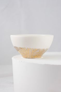 a white and gold bowl sitting on top of a white table next to a gray wall