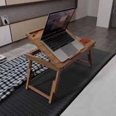 an open laptop computer sitting on top of a wooden table next to a bed with blue and white checkered bedspread