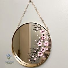 a mirror hanging on the wall with flowers painted on it and chain attached to it