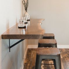 a wooden table with two stools next to it and a vase on the wall