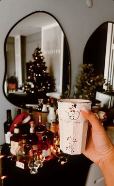 a person holding up a cup in front of a christmas tree and other holiday decorations