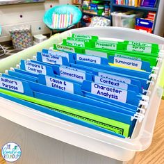 a plastic container filled with lots of folders on top of a wooden table in front of a bookshelf